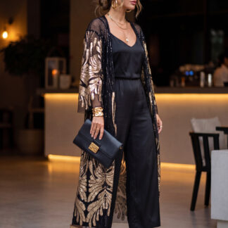 Black sheer sequin kimono with gold leaf pattern. Styled as elegant evening wear over a black jumpsuit, accessorized with gold jewelry, sunglasses, and a black clutch bag in a restaurant setting.