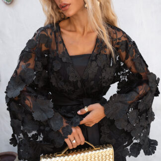 Close-up of a black sheer mesh kimono featuring large 3D floral appliques and a gold woven clutch, highlighting the romantic flower texture.